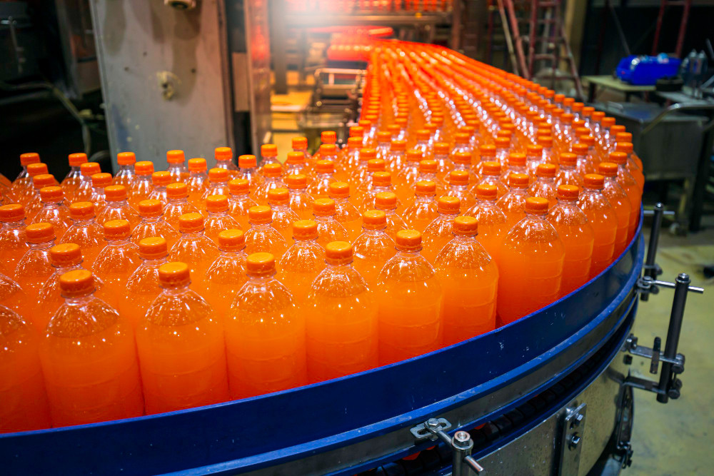 Linha de envase em indústria de alimentos e bebidas, com garrafas sendo transportadas em esteira industrial automatizada